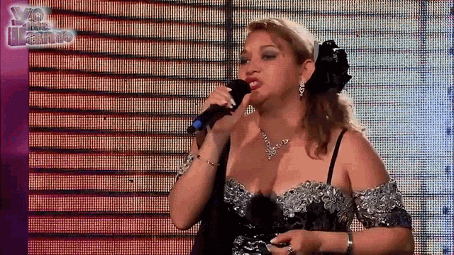a woman sings into a microphone in front of a screen that says yo me llama