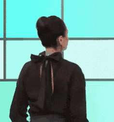 a woman in a black shirt with a bow on the back is standing in front of a blue wall .