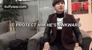 a man is sitting in a chair with a bottle of water in front of him and says protect him he 's awkward