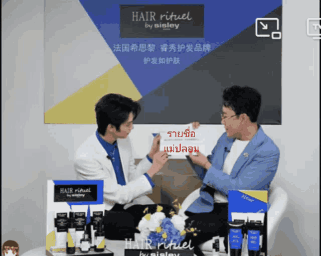 two men sitting in front of a sign that says hair ritual by sisley