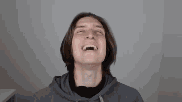 a young man with long hair is laughing with his mouth open