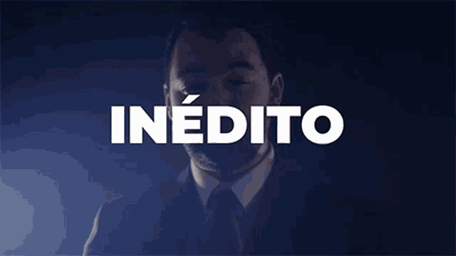 a man in a suit and tie stands in front of a sign that says inedito