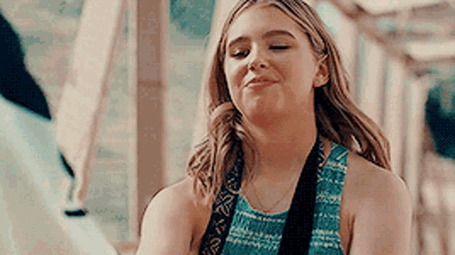 a young woman in a blue tank top is smiling while holding a guitar strap .
