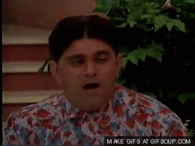 a man in a floral shirt is sitting in front of a plant and stairs