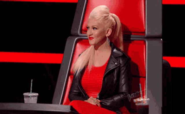 a woman in a red dress and black leather jacket sits in a chair with a starbucks cup in front of her