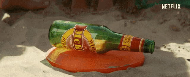 a bottle of mom beer is laying in the sand on a frisbee
