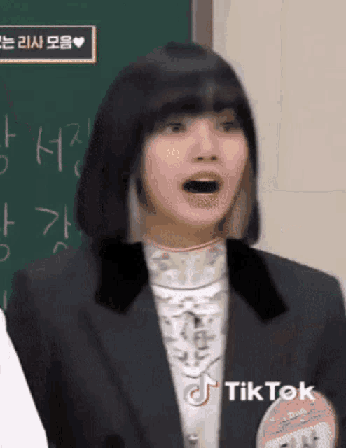 a woman in a suit is standing in front of a blackboard with her mouth open