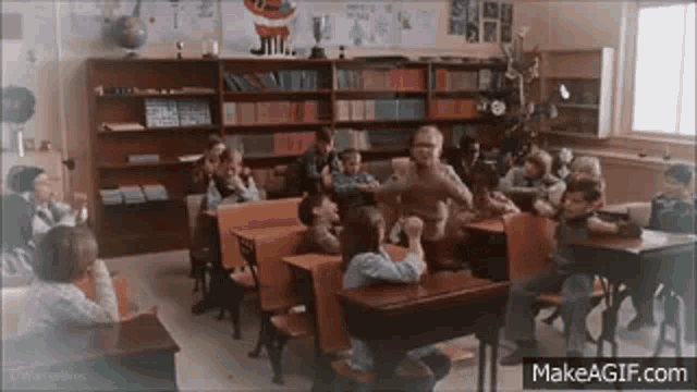 a group of children are sitting at their desks in a classroom with a santa claus poster on the wall .