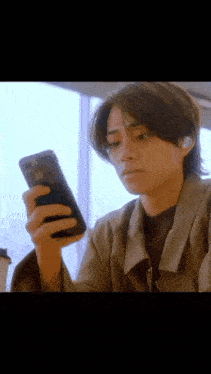 a young man is looking at his cell phone while sitting at a table .