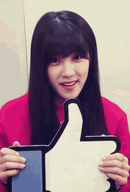 a girl in a pink shirt is holding a facebook like sign