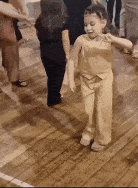 a little girl is dancing on a wooden floor with other children