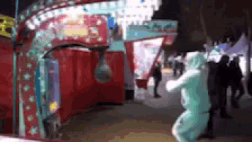 a man in a blue jumpsuit is standing in front of a carnival ride .