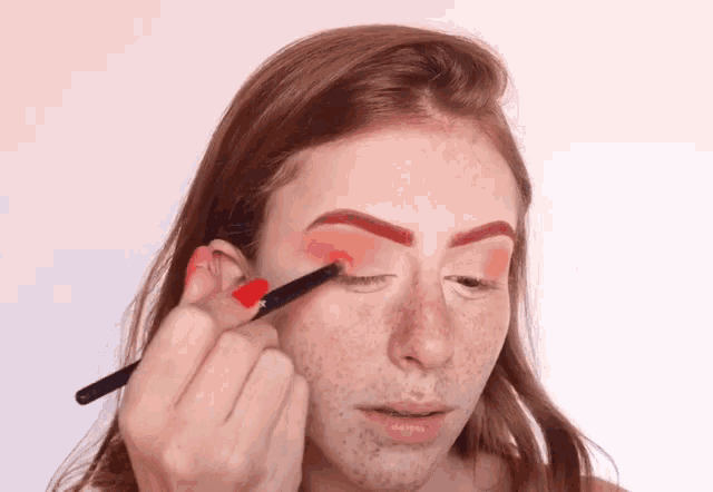 a woman is applying makeup to her eye with a brush .