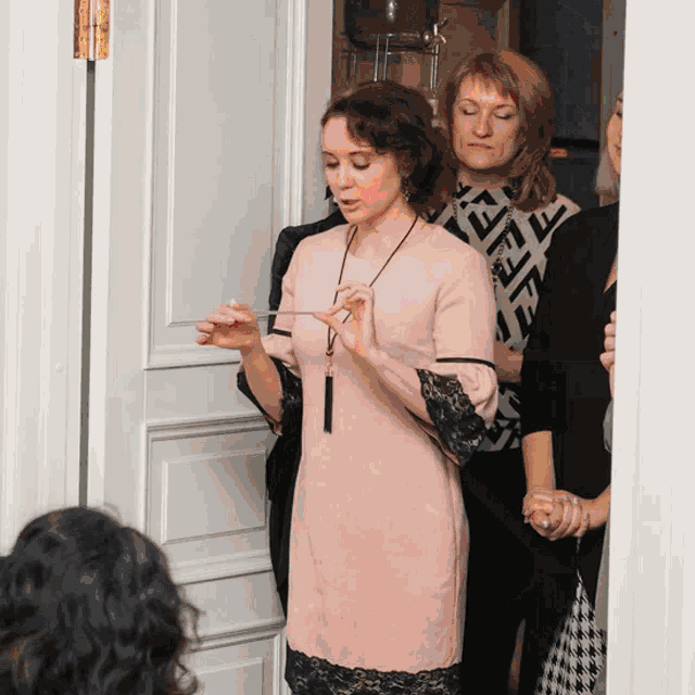 a woman in a pink dress stands in front of a door with a woman in a fendi shirt behind her
