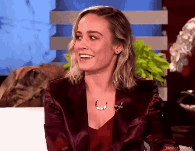 a woman wearing a purple jacket and a necklace is smiling