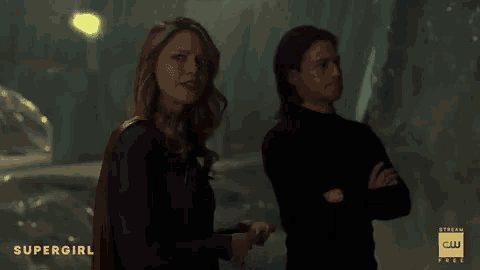 a woman in a supergirl costume is standing next to a man in a black shirt