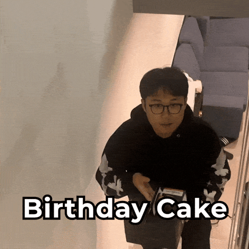 a man wearing glasses holds a birthday cake