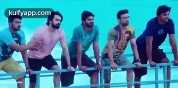 a group of men are leaning on a railing in front of a swimming pool .