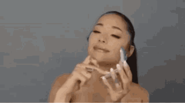 ariana grande is applying makeup to her face while looking at herself in a mirror .