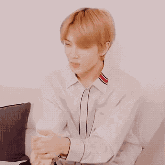 a young man is sitting on a couch with his hands folded in front of his face .