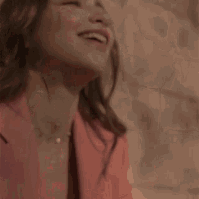 a woman wearing a pink jacket and a necklace is laughing