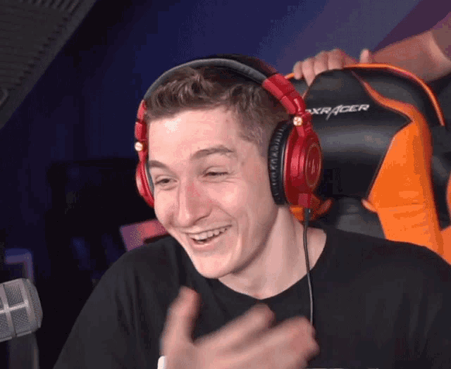 a man wearing red headphones is sitting in an orange and black dxracer chair
