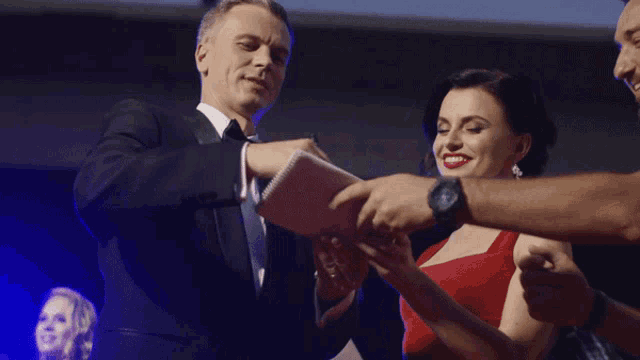 a man in a tuxedo is giving a woman a notepad