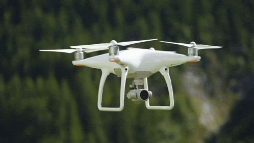 a white drone with a camera attached to it is flying over a forest