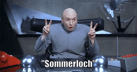 a bald man sitting at a desk giving a peace sign with the word sommerloch below him