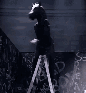 a man with a horse head is standing on a ladder in front of a blackboard .