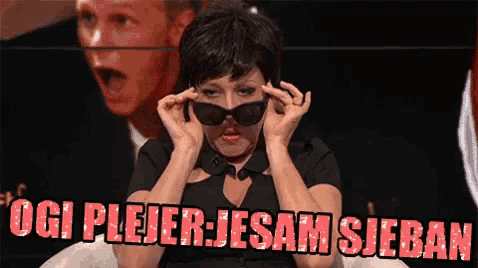a woman wearing sunglasses is sitting in front of a sign that says ' oigi plejer jesam sieban '