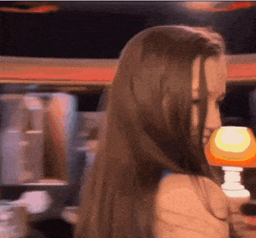 a woman with long brown hair stands in front of a lamp
