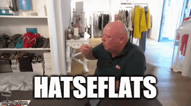 a bald man is sitting in a room with the words hatseflats behind him