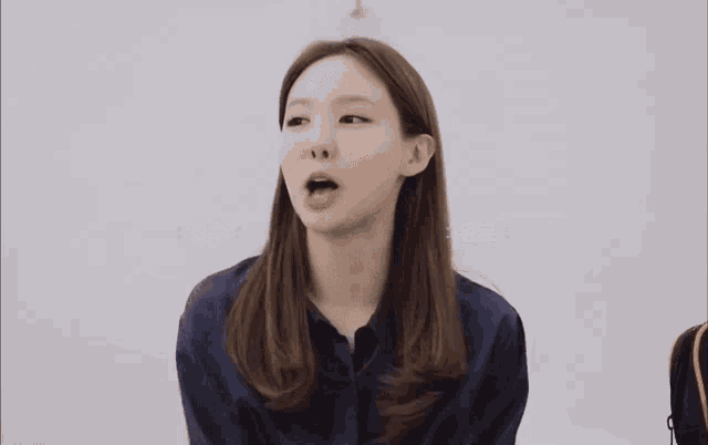 a woman in a blue shirt is smiling in front of a white wall