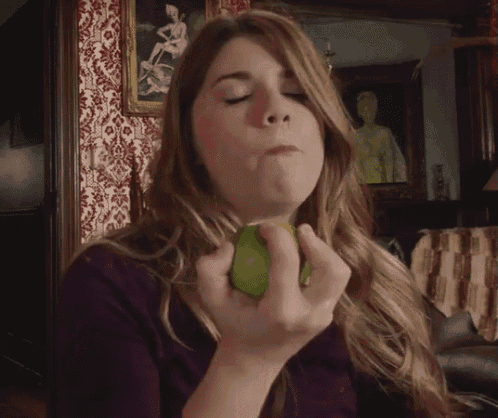 a woman in a purple shirt is eating a green pear