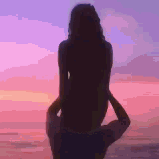 a silhouette of a woman sitting on a man 's shoulders at sunset .