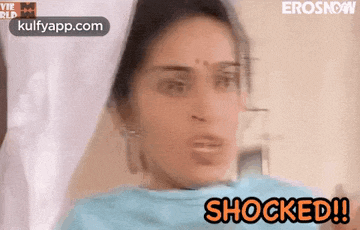 a woman is sitting on a bed and looking at the camera with the words shocked written above her .