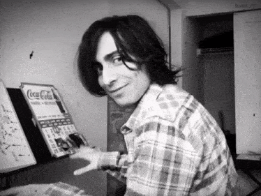 a man in a plaid shirt is playing a piano in front of a coca cola sign