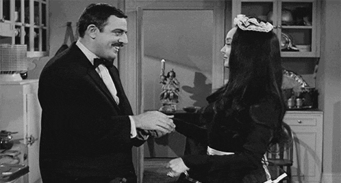 a man in a tuxedo and a woman in a maid costume are standing next to each other in a kitchen .