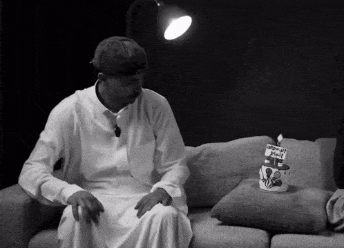 a black and white photo of a man sitting on a couch next to a birthday cake that says happy birthday