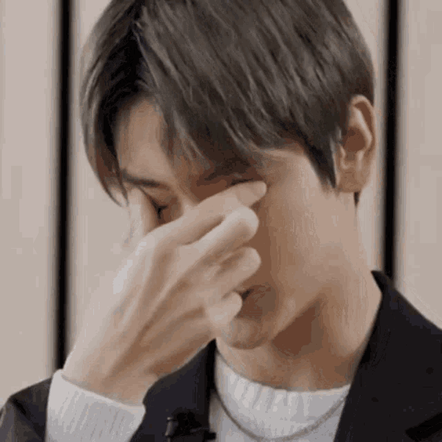 a man in a suit is covering his face with his hand .