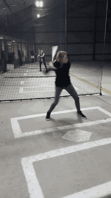 a girl is swinging a bat at a baseball in a cage