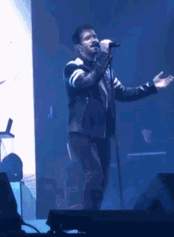 a man in a leather jacket singing into a microphone on stage