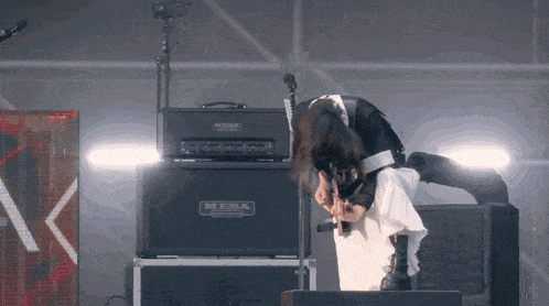 a woman is playing a guitar in front of a mesa amplifier