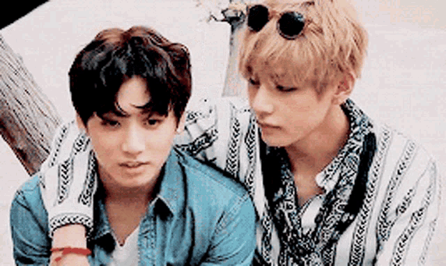 two young men are sitting next to each other wearing sunglasses and shirts .