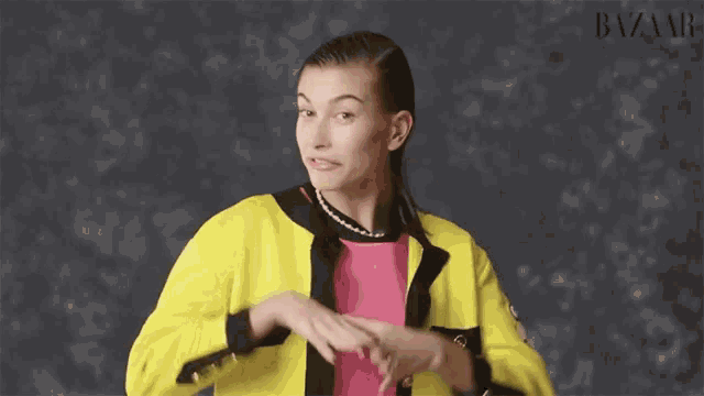 a woman wearing a yellow jacket and a pink shirt is making a heart shape