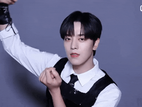 a young man in a white shirt and black vest making a heart shape with his hands