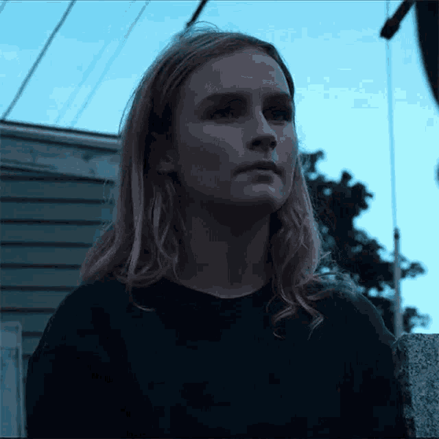 a woman with long blonde hair is wearing a black sweater and standing in front of a building .