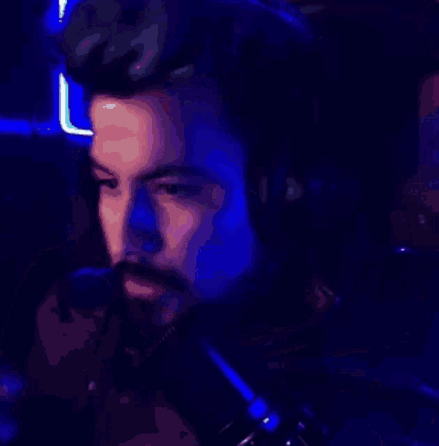a man with a beard is wearing headphones in a dark room with blue lights behind him