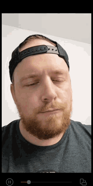 a man with a beard wearing a black hat and a grey shirt